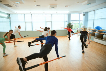 Male coach showing group of people balancing with gymnastic sticks