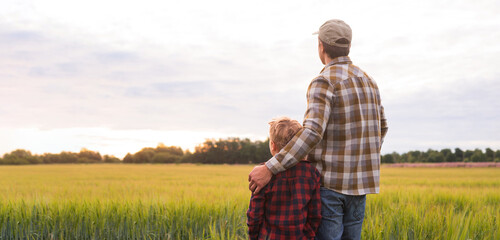 Farmer and his son in front of a sunset agricultural landscape. Man and a boy in a countryside field. Fatherhood, country life, farming and country lifestyle concept.