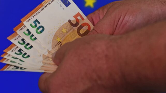 Counting fifty euro notes with blue flag background in city setting
