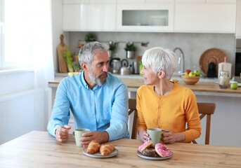 A man and a woman are smiling and holding cups of coffee in a kitchen. Scene is happy and friendly