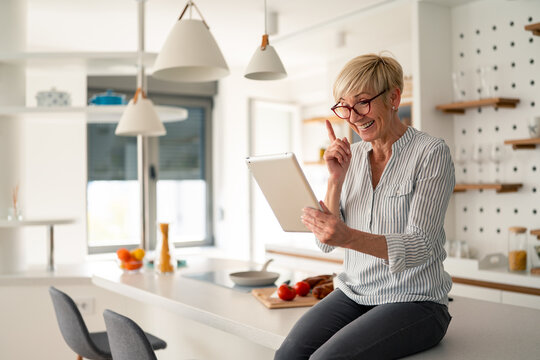 Senior Woman Smiling and Working on Tablet in Bright Modern Kitchen at Home