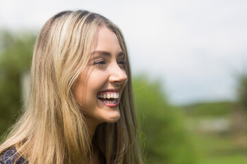 Naklejka premium Woman laughing and looking right in park, showing long blonde hair, teeth, wearing dark top