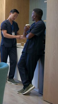 Vertical video: Making coffee, two staff in navy scrubs moving into lounge for break, holding cups