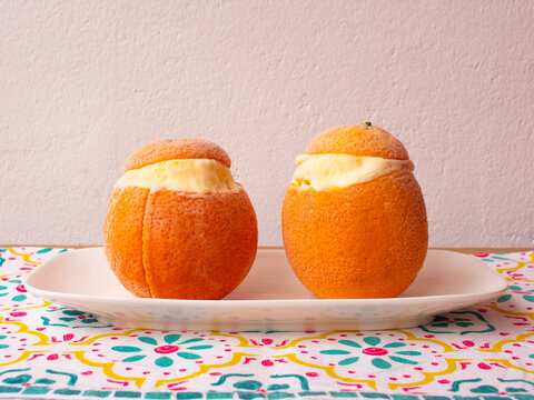 Dos naranjas rellenas de helado de naranja sobre plato blanco y mantel colorido