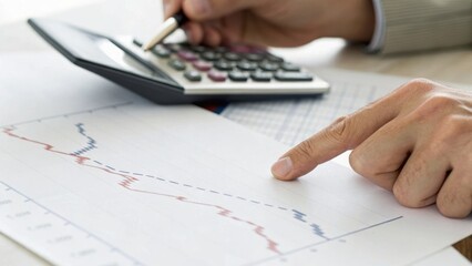 A person analyzing financial data with a calculator and graph, indicating a downward trend on the paper.