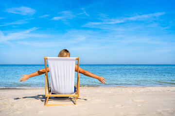 Mature woman relaxing on white sandy beach sitting on deckchair on seashore in summertime. Back view © Jacek Chabraszewski