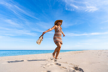 Fototapeta premium Happy summer vacations. Beautiful middle-aged woman tourist spinning around on white sandy beach on beautiful sunny day