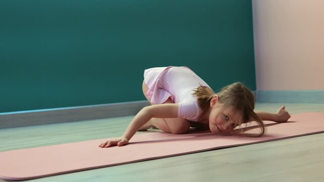 Young girl practicing neck and upper back mobility exercise on mat in fitness studio, practicing flexibility and body control