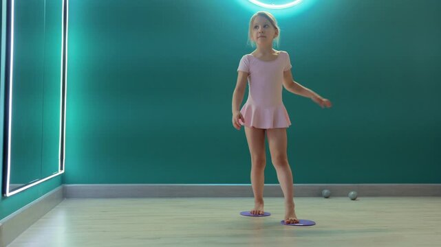 Young girl is practicing balance and coordination on gliding discs in fitness studio, training stability and body control