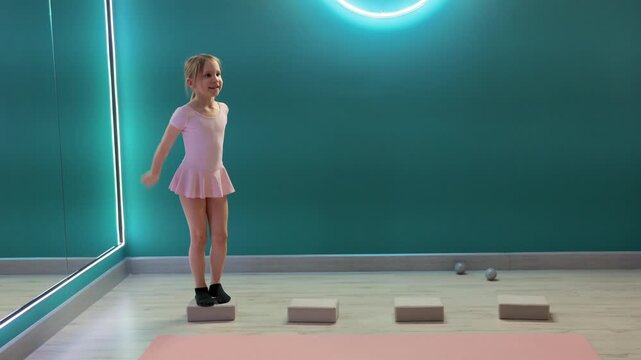 Young girl is stepping across foam blocks while tossing and catching ball in fitness studio, practicing balance, coordination, and agility
