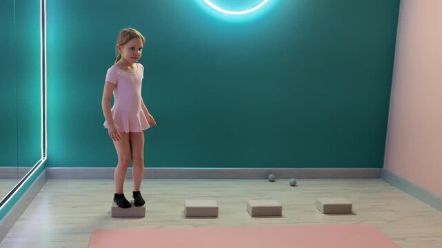 Young girl is practicing balance and coordination by stepping across foam blocks in fitness studio, training footwork and stability