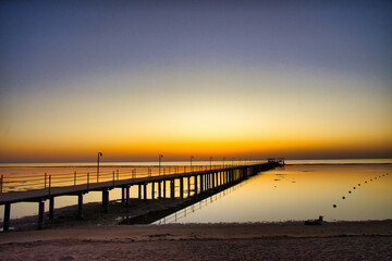 Obraz premium A breathtaking sunset over the Red Sea in Egypt, with a long wooden pier stretching across calm, reflective water.