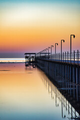 Obraz premium A breathtaking sunset over the Red Sea in Egypt, with a long wooden pier stretching across calm, reflective water.