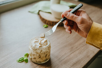 Close up of male hand tasting tofu from jar on a wooden table
