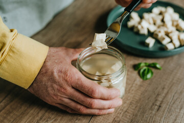 Males hands holding tofu on a fork over a jar