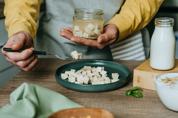 Males hands holding tofu on a fork over a jar