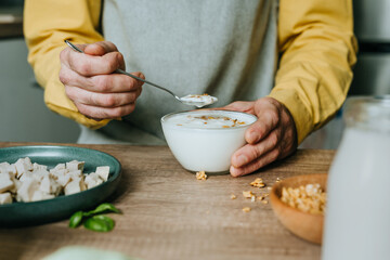 Man eating yogurt with granola in bowl on wooden table