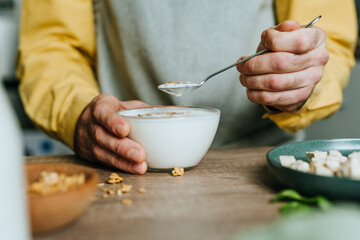 Man eating yogurt with granola in bowl on wooden table
