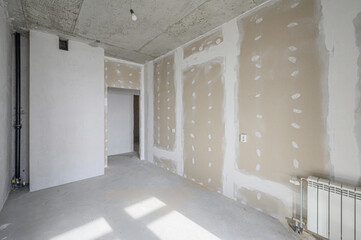 Unfinished room with plastered walls, exposed concrete ceiling, bare floor, radiator, electrical...