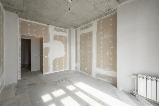 Unfinished room with plastered walls, exposed concrete ceiling floor, radiator installed, doorway open, patchy drywall, awaiting final finishing touches.