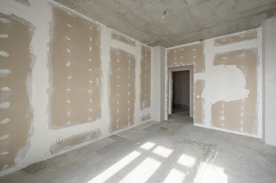 Unfinished room with gypsum board walls, exposed concrete ceiling and floor, electrical outlet visible, doorway open, awaiting final plastering and painting.