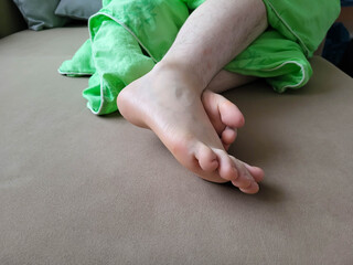 On a bed, at the feet of a sleeping person, covered with gray bedding and a green blanket