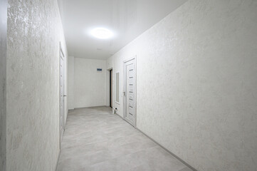 Light-toned hallway with textured wallpaper, light grey tiled floor, white doors with horizontal panels, recessed ceiling light, minimal decor, neutral palette, clean lines.