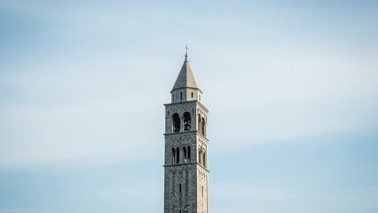 Obraz premium Tall stone bell tower rises majestically against clear blue sky. Historic bell tower architecture features intricate details, classic arched windows, and pointed spire.