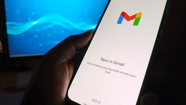 A hand holding a smartphone with the Gmail app open in a dark room