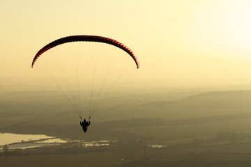 Freedom and adventure concept. Silhouette of a paraglider flying against a golden sunset sky.