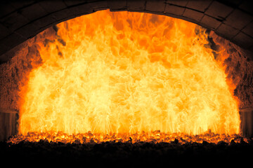 Inside view of an industrial furnace with roaring orange flames and glowing coal.