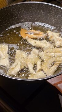 Angel wings pastry faworki frying in hot boiling oil inside pan for traditional Polish Fat Thursday celebration delicious homemade sweet crispy dessert. Cooking process. Video 4k