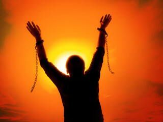 Silhouette of man against the sunset sky raising up his hands as he becomes free from chains and shackles