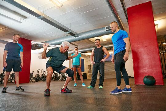 Coach, old man and squat in gym with pipe for mobility exercise, physical activity or wellness. Personal trainer, senior person or pvc equipment with advice for workout, stability or fitness support.