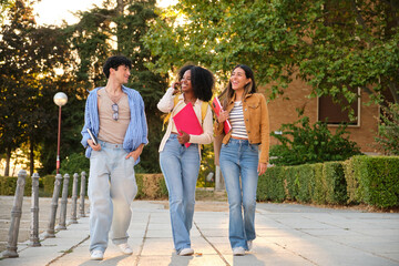 Fototapeta premium Group of diverse university students walking campus together smiling and talking, holding notebooks