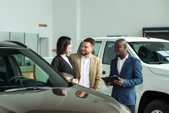 Group of three diverse individuals discussing car features inside a modern automotive showroom with vehicles prominently displayed in the background