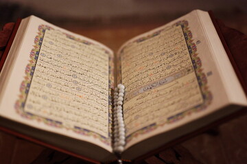 Fototapeta premium Close-up of open Quran pages with prayer beads in warm ambient lighting