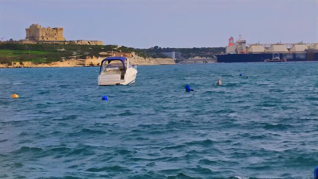 Motorboat on choppy sea in front of LNG tanker and limestone cliffs in Birzebbuga, Malta