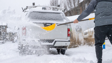 Individual shoveling snow from a vehicle in a winter landscape, showcasing the effort required during a snowstorm for vehicle accessibility
