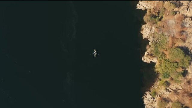 Aerial reveal shot of rocky cliffs and the Nile River as drone ascends over a rowing boat, Aswan, Egypt