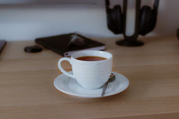 Cup of tea on saucer on home desk with notebook and headphones