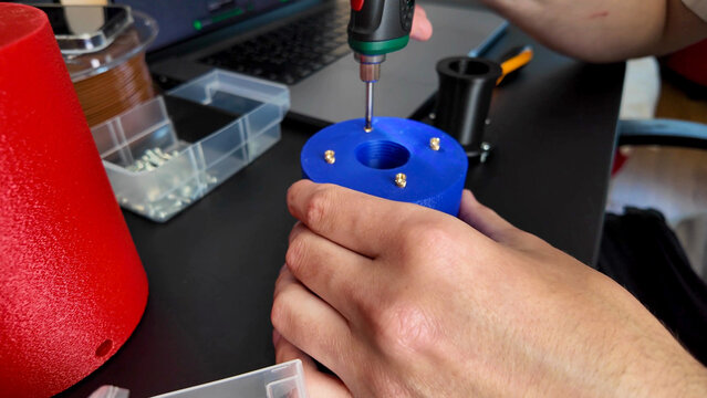 Hands meticulously assemble vibrant blue device in home workshop, embodying DIY ingenuity, akin to National Inventors Month creativity