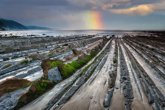 Flysch of Zumaia with rainbow and geological formations at sunset, spain