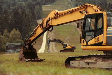 A large yellow hydraulic excavator parked on a grassy hillside. Undergoing construction or land modification. Preparing terrain for snowmaking infrastructure