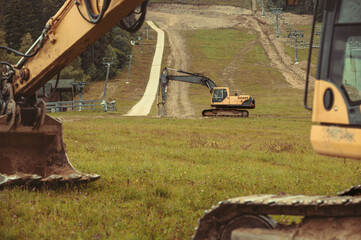 A large yellow hydraulic excavator parked on a grassy hillside. Undergoing construction or land...