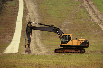 A large yellow hydraulic excavator parked on a grassy hillside. Undergoing construction or land modification. Preparing terrain for snowmaking infrastructure