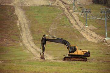 A large yellow hydraulic excavator parked on a grassy hillside. Undergoing construction or land modification. Preparing terrain for snowmaking infrastructure