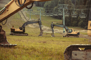 A large yellow hydraulic excavators parked and serviced on a grassy hillside. Undergoing construction or land modification. Preparing terrain for snowmaking infrastructure