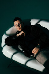 Fototapeta premium A portrait photo of a male model in a dark studio with window light. The handsome man wearing glasses looks into the camera. The businessman and his fashionable, elegant style