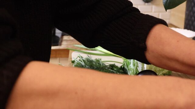 Close-up footage of a woman slicing fresh green vegetables on a wooden kitchen countertop while a domestic cat sits nearby. Cozy home cooking scene, healthy food preparation and everyday lifestyle wit